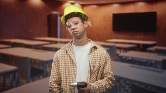 Man holding drill and wearing hardhat as construction worker in classroom, slouched posture and vacant gaze; work weariness.