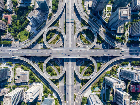 Aerial view of a complex urban cloverleaf interchange with multiple highway lanes and city skyscrapers in a modern metropolitan environment.