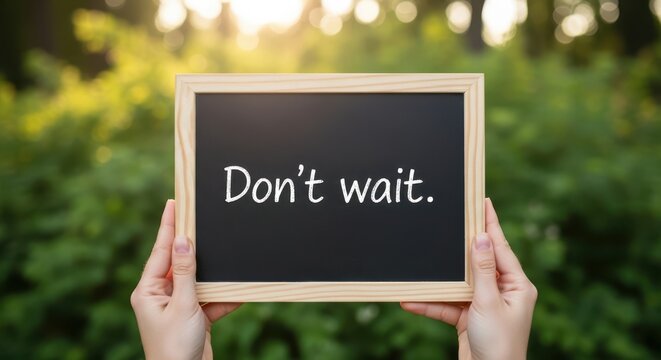 Hands holding a chalkboard with the text dont wait written on it against a blurred green nature background