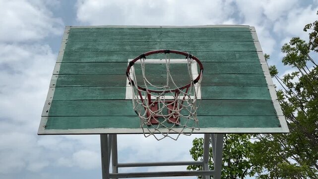 Old outdoor basketball hoop on a green wooden backboard under a clear blue sky. 