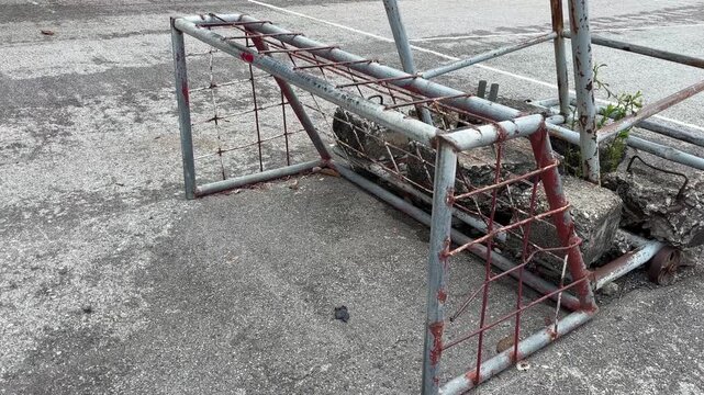 Old rusty steel futsal goal on a quiet street court with worn metal texture under natural daylight.