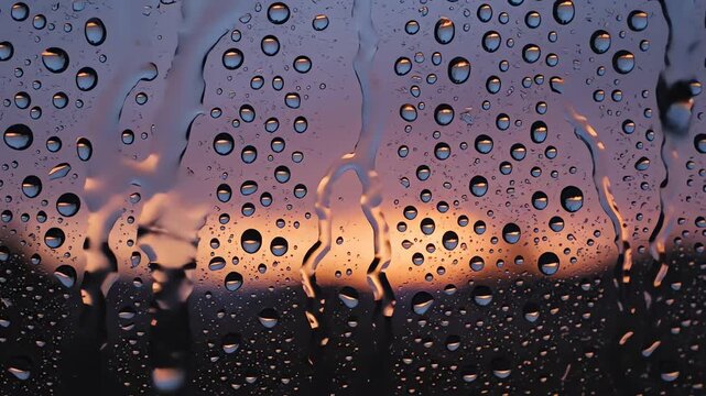 Raindrops on window pane with orange sunset horizon