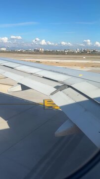 Passenger&rsquo;s view from airplane window as the plane taxis on the runway, wing visible while preparing for takeoff with airport surroundings and runway lights.