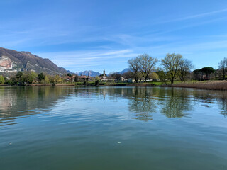 Fototapeta premium Peaceful view near Lake Pusiano with calm water, mountain scenery, and reflections under a bright blue sky, capturing serenity, nature, and Italian countryside charm.
