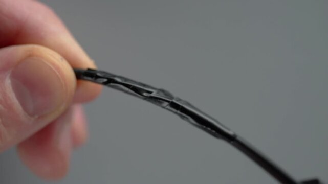 Closeup caucasian hands heating wire insulation with lighter, shrinking black tubing around exposed conductor, visible flame, delicate grip, DIY repair demonstration, cautionary
