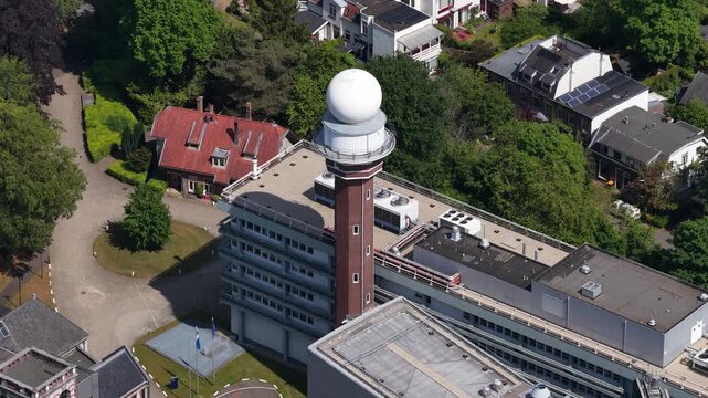 Aerial perspective of a meteorological radar dome on a tower at a weather forecasting center. Slowly rotating to provide a comprehensive view of the surrounding residential area and lush green trees