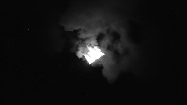 Black and white shot of a bright flame and billowing smoke against a starry night sky