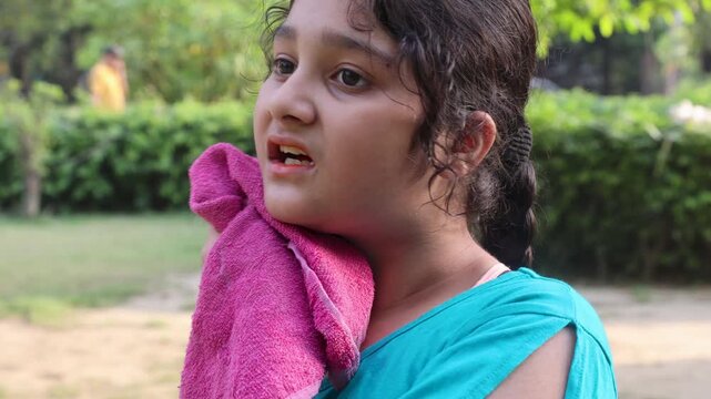 Close view of a young Indian girl using a cloth to clean sweat from her face during extremely hot summer weather in a green park. Outdoor heat and lifestyle moment captured in India.