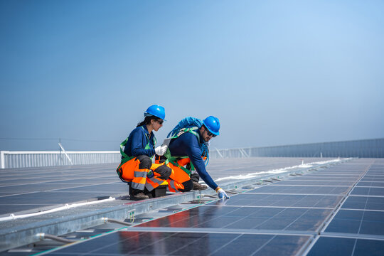 Engineers team installing and inspecting solar panels on rooftop with safety equipment, Maintenance worker team in high-visibility uniform working on solar power station under blue sky