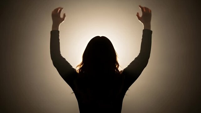 Silhouetted woman raises hands upward against a glowing background, backlit figure
