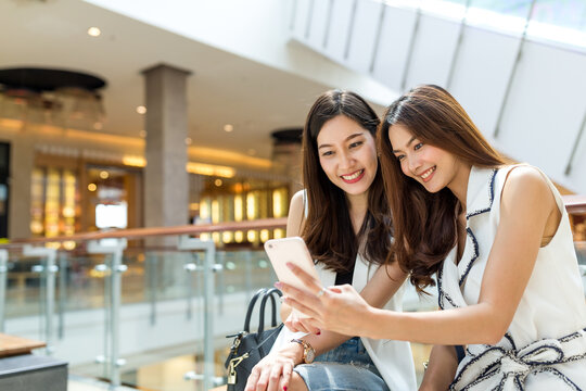 Asian women looking at photos on a smartphone while sitting indoors