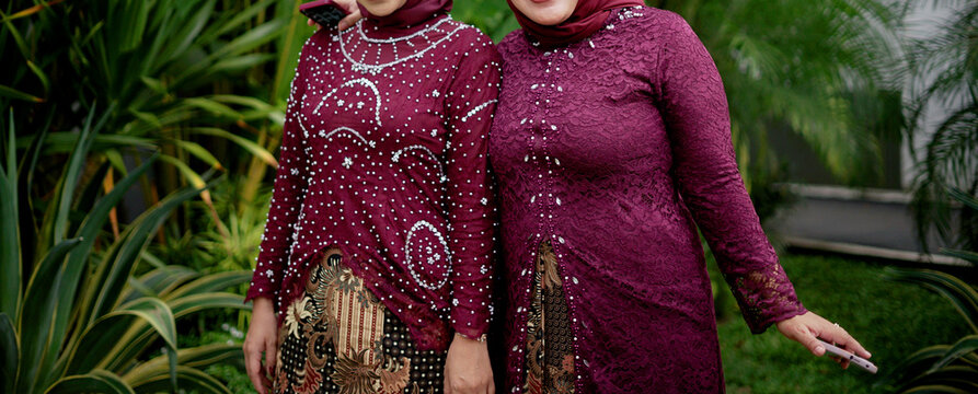 Two faceless female bodies wearing burgundy kebaya with beautiful batik cloth, standing in a green garden