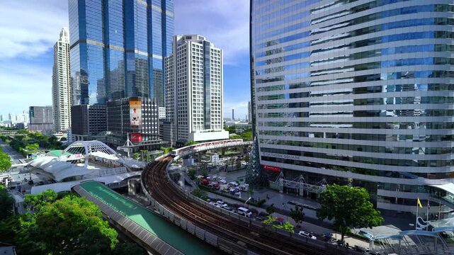 High-angle time-lapse of a BTS Skytrain navigating a dramatic curved track surrounded by modern skyscrapers and corporate office buildings at the Chong Nonsi intersection in Sathorn, Bangkok, Thailand