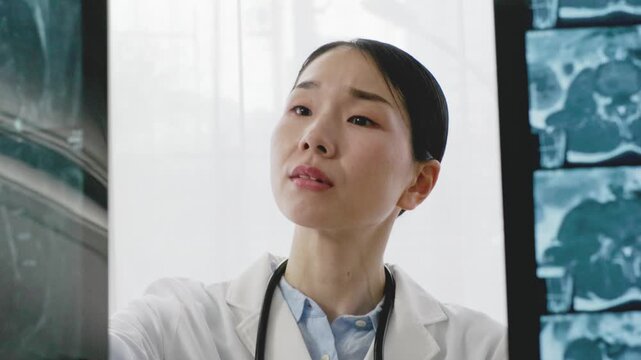 Asian Female Doctor in White Coat Reviewing X-ray Image