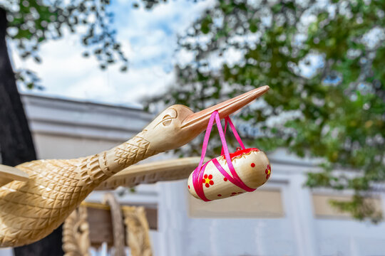 A wooden model of a stork holding a baby in its beak.