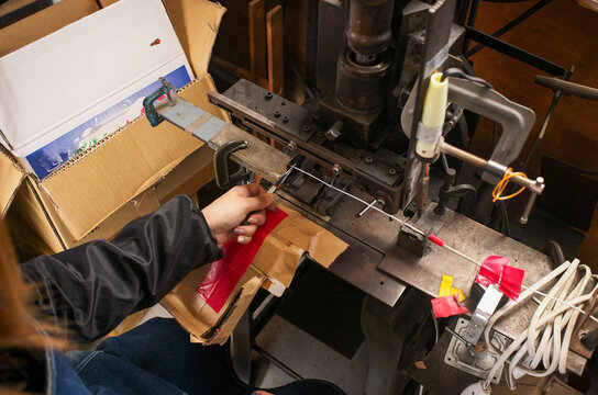 Worker operating vintage flywheel press machine for precision lead wire processing in small factory