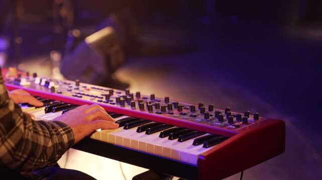 Musician playing an electric synthesizer during a concert. Close-up of male hands playing a keyboard musical instrument.