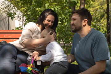 Fototapeta premium Happy parents with their adorable baby sitting on bench in park