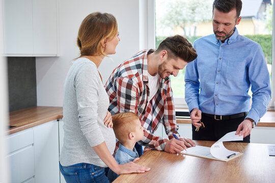 Family with real estate agent signing contract in kitchen of new apartment