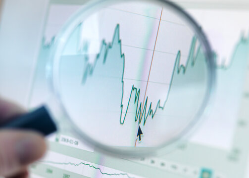 Investor analysing line graph on computer screen with magnifying glass