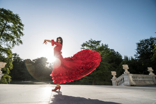 Woman dressed in red dancing flamenco on terrace at backlight