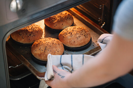 Woman taking homemade vegan burger rolls out of oven