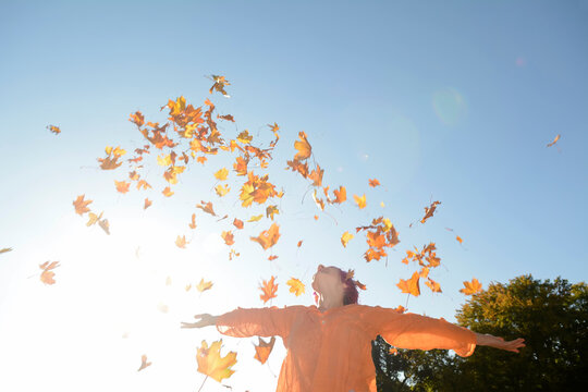 Young woman throwing autum leaves in the air