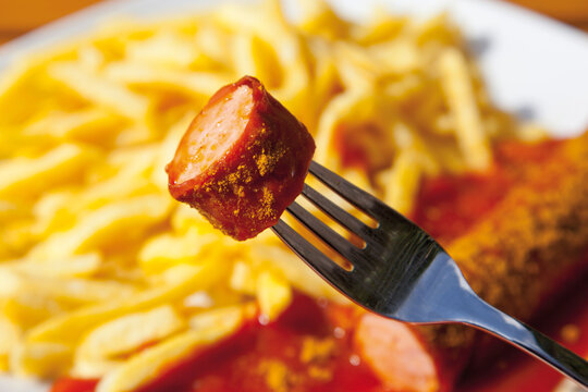 Curry sausage on fork with chips in background