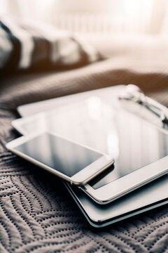Stack of three mobile devices on bed
