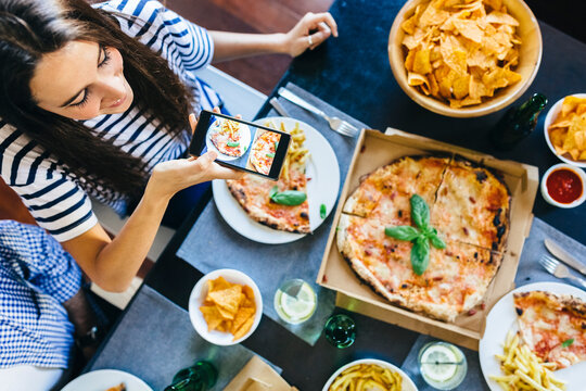 Woman taking cell phone picture of pizza on table