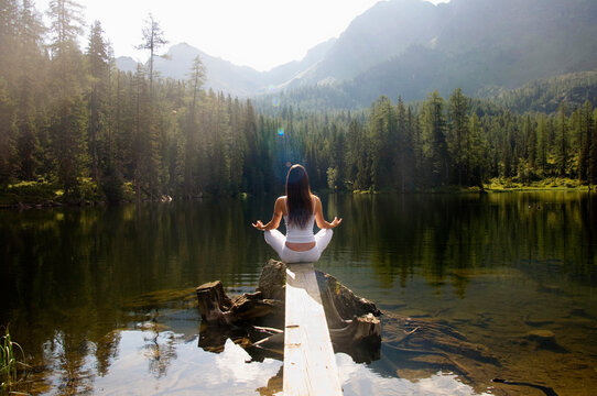 Woman exercising yoga at lake, rear view