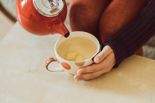 Woman pouring water into tea cup with chopped fresh ginger, close-up