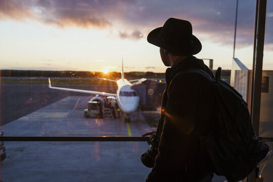 Young man with hat and backpack looking through window on plane at the airport