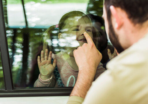 Father touching girl's nose behind car window