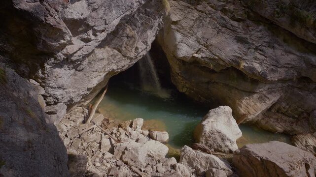 Hidden waterfall in Starzlachklamm gorge, inside a dark cavern with blue-green water pool.
