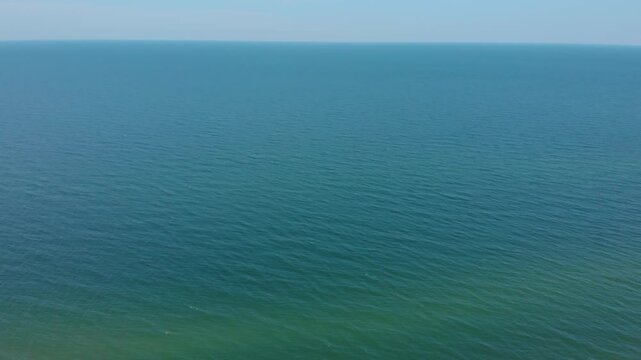 An aerial drone shot capturing the vast, tranquil expanse of the Baltic Sea. The footage features a gradient of deep turquoise and blue water meeting a clear, pale blue sky at the horizon.