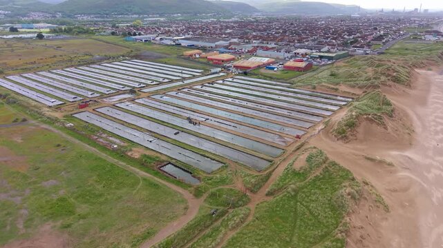 Aerial Orbit View of Commercial Ragworm Farm and Marine Bait Production. Sediment beds and water filtration systems used to cultivate ragworms for the global fishing bait market. United Kingdom. 4K.