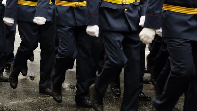 Close-up of uniformed personnel marching in synchronized formation during a ceremonial parade, with disciplined steps, white gloves, navy attire, and footwear on wet pavement.