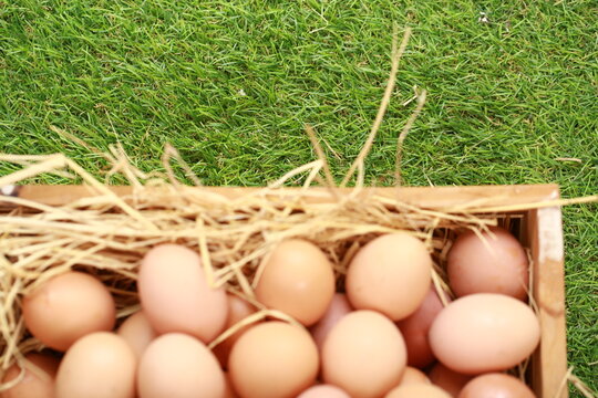 A high-angle, close-up shot shows a cluster of smooth, brown chicken eggs packed inside a cream-colored textile pouch. The bag is gathered at the edges, resting on a warm, dark wood surface. The light