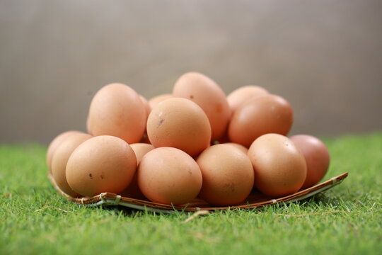 A high-angle, close-up shot shows a cluster of smooth, brown chicken eggs packed inside a cream-colored textile pouch. The bag is gathered at the edges, resting on a warm, dark wood surface. The light