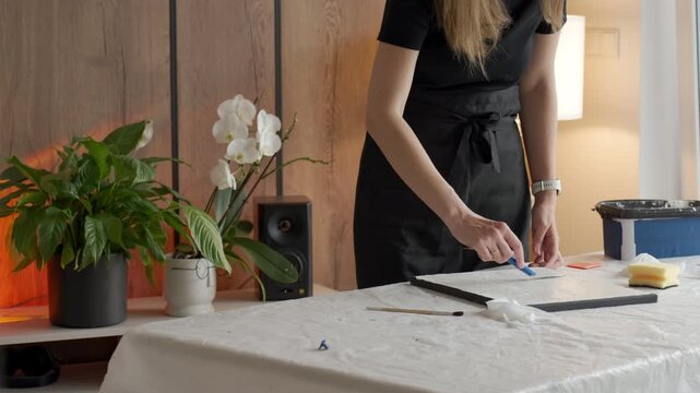 Female artist shapes white plaster paste on black canvas at a protected table. Concept of abstract textured art, handmade decor and creative process.