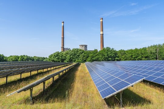 Solar modules of a solar park in front of the decommissioned Plessa lignite-fired power plant with two chimneys and cooling towers, Plessa, Lusatia, Brandenburg, Germany