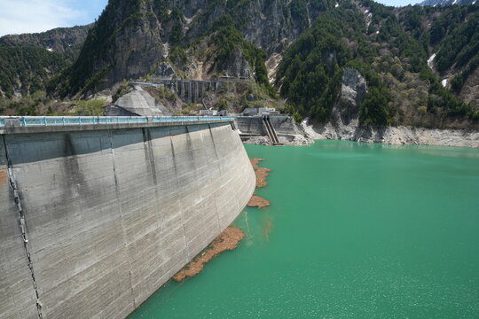 A massive concrete wall of Kurobe Dam with emerald water.