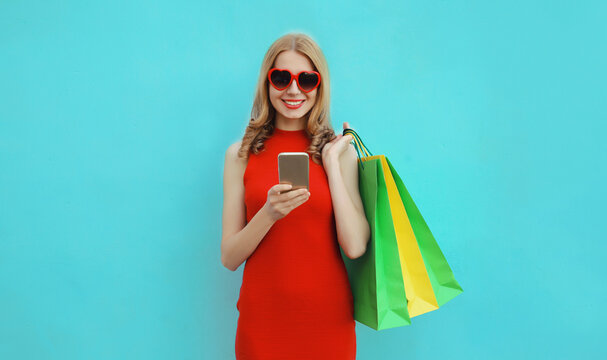 Beautiful happy young woman holding phone with colorful shopping bag on studio background