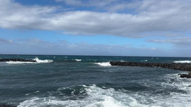 Powerful Atlantic surf crashes into black volcanic rocks along a rugged island shoreline under dramatic clouds. Natural seascape with white foam, spray, and deep blue water.