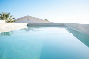 Fototapeta premium Bright blue swimming pool surface reflecting clear sky near a modern white building edge