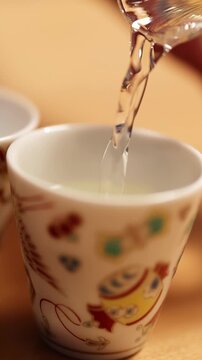 Clear Japanese Sake Pouring into a Traditional Decorated Ceramic Ochoko Cup