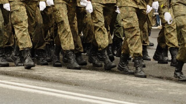 Close-up view of uniformed soldiers in camouflage fatigues marching in tight formation with black combat boots along a city street during a military parade drill