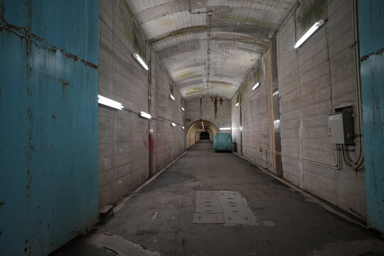 Symmetrical perspective of an underground concrete tunnel with fluorescent lights.