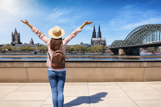 A happy tourist woman with a backpack looks at the panoramic skyline of Cologne, Germany